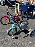 Photo of both bikes together on pavement outdoors, showing pink bike with training wheels and turquoise tricycle close up.