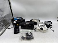 Overview of multiple cameras, cases, charger, cables on white background