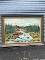 Full view of framed landscape painting showing river, rocks, trees, and mountains with the frame included.