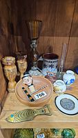 Shelf with a grouping of small decorative and collectible items including carved wooden owls, candle holder, ceramic crock, and other small decorative pieces.