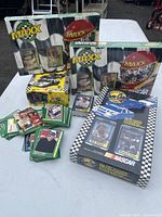 Photo of the four unopened Maxx NASCAR trading card boxes and loose trading cards displayed on a white table outdoors.
