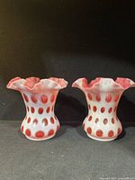 Front view of pair of Fenton cranberry coin dot vases with double crimp ruffle tops on a black background.