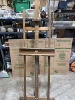 Full front view of the tall wooden easel showing general shape and assembly with shelf and adjustment rail.