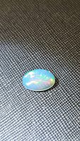 Oval cabochon natural Ethiopian opal gemstone placed on a textured black surface showing multicolored flashes of color including green, yellow, and red hues.