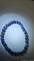 Blue sodalite bead stretchy bracelet laid flat on a surface, showing round polished blue beads with white-grey marbling.