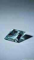 Lozenge cut aquamarine gemstone on white background, angled view showing top facets and color