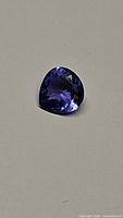 Image showing the pear-shaped deep blue/purple Tanzanite gemstone on a plain background highlighting its clarity and color.
