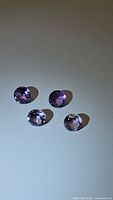 Four round cut natural amethyst stones shown from above on a flat surface under direct light.