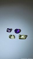 Four loose gemstones laid out on a neutral surface under bright lighting showing deep purple amethysts and pale yellow lemonade citrines in two shapes each.