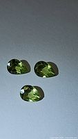 Three pear-shaped apple green peridot gemstones laid on a light surface, showing facets and color.