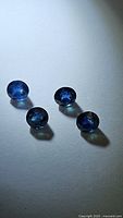 Four natural round cut blue sapphires on white background under soft lighting showing color and transparency.