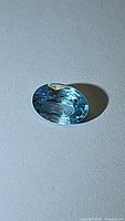 Oval cut seafoam blue natural zircon gemstone photographed on a light surface showing its color and clarity.