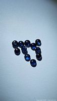 Photo showing 14 round deep blue natural sapphires scattered on white background with light reflection highlighting the rich blue color.