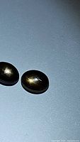 Close-up of pair of oval cabochon-cut black star sapphires showing golden star effect on blue background.