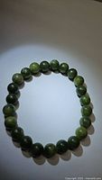 Natural green jade stretchy bracelet laid flat showing round polished beads in various shades of green.