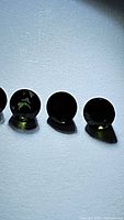 Four round calibrated green tourmaline gemstones displayed in a row on a white background with light reflection showing green color and faceting.