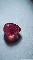 Close-up of the natural ruby gemstone showing the faceted briolette cut and drilled hole.