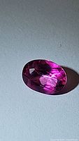 Close-up photo of the oval faceted natural hot pink topaz with vivid pink color and visible internal clarity and color saturation.