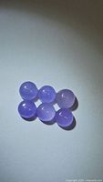 Six round lavender purple chalcedony cabochon gemstones arranged closely on a white background, displaying their smooth polished dome surfaces and consistent color.