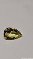 Pear cut natural lemon citrine gemstone shown on neutral background, displaying size, color and cut details.