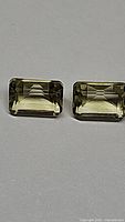 Pair of natural lemon citrine emerald cut gemstones placed side by side showing their matching size, cut, and color tone.
