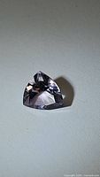 Light pink natural amethyst gemstone with trillion cut, shown from one angle on a neutral background.