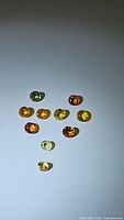 Twelve small faceted natural sapphires of varied rainbow colors arranged on a white surface under direct light.