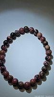 Photo showing natural rhodochrosite 6mm bead stretchy bracelet with mixed pink, brown and black tones forming distinctive patterns.