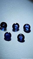 Five round cut natural royal blue Ceylon sapphires approximately 3.5mm each, with high clarity, under direct lighting showing facets and depth of color.