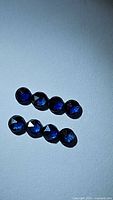 Eight natural royal blue round fancy rose cut sapphires arranged in two rows on a plain light surface, showing facets and deep blue color.
