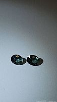 Pair of oval-cut natural sapphires with bright aqua blue-green color on a light background.