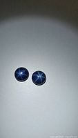 Two round blue star sapphire cabochons shown together on a plain background, clear six-ray star effect visible.