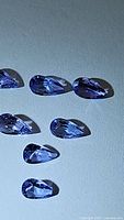 Seven pear-shaped natural tanzanite gemstones arranged on a surface, showing color and clarity under light.