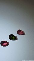 Three natural tourmaline gemstones in pink and green colors displayed against white background in mixed cuts showing pear and oval shapes.