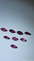 Eight marquis cut deep pink to red rubies arranged on flat surface showing size and color variations.