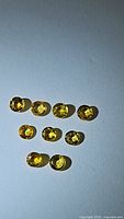 Nine round-cut natural yellow sapphire gemstones arranged in a diamond formation on a flat surface under direct light, showing their color and facets.