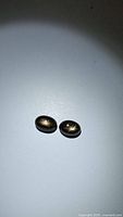 Pair of oval black star sapphire gemstones under direct light showing golden 6-ray star effect.