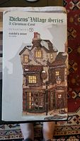 Image of box packaging showing the Department 56 Dickens' Village Series Cratchit's Corner building with product information and image.