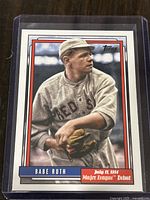 Front view of Topps baseball card depicting Babe Ruth in Boston Red Sox uniform, dated July 11, 1914, sealed in plastic sleeve.