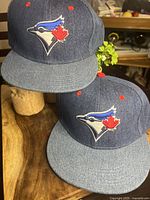 Two blue denim Toronto Blue Jays snapback hats displayed on a wooden surface, showing front and side views featuring embroidered team logo.