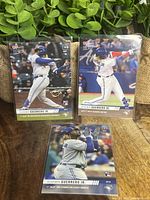 Three 2019 Topps Now Vladimir Guerrero Jr baseball cards in protective sleeves laid out on table with potted plants in background. Cards depict key milestones of his May 2019 debut.
