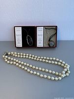 Two ammonite fossil necklaces in individual boxes next to a pearl-like beaded necklace laid out below them on a light background.