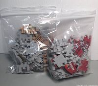 Two zip-lock bags containing disassembled 3D puzzle pieces colored and printed to depict parts of a red London phone booth and other architectural components.