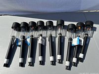 Nine black solar LED landscape garden lights with clear covers, arranged in a row on a surface in sunlight.