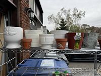 Full view of all assorted plant pots on a metal rack, showing variety of sizes, colors, and materials.