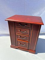 Front view of a wooden jewellery box with 4 drawers and decorative brass handles.