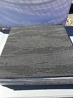 Single sample carpet tile showing textured dark gray linear pattern and size 50 cm by 50 cm.
