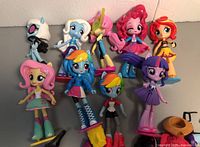 Nine colorful Equestria Girls dolls arranged standing upright showing variety of characters and vibrant clothing and hair colors.