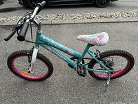 Side view of Fly Girl by Supercycle girls bike, showing teal frame, pink rims, tires, hand brakes, and decorative seat