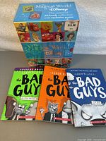 Three individual books from The Bad Guys series by Aaron Blabey (books 1, 7, and 9) with colorful covers in front of the Disney collection box.